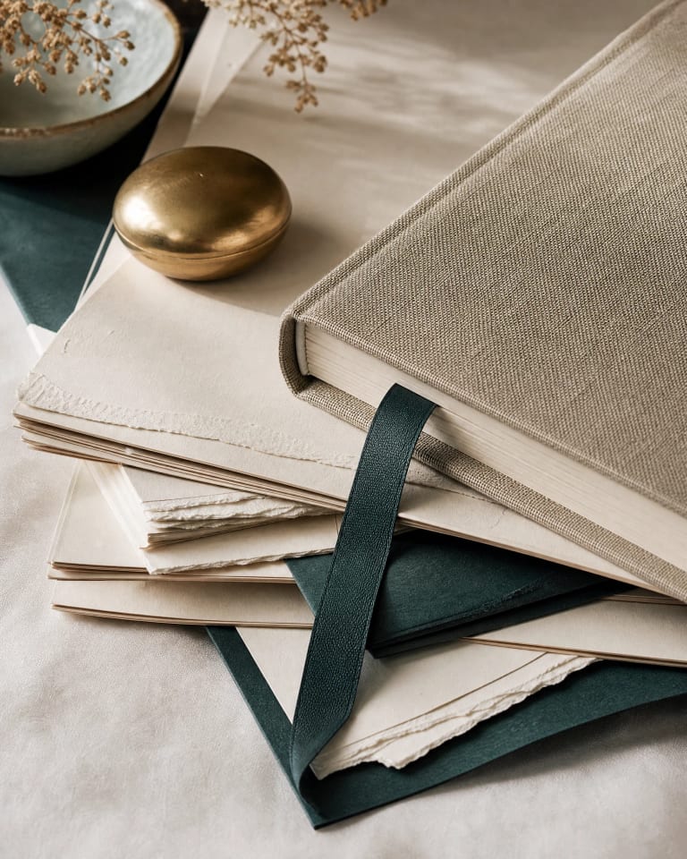 A linen-bound planning book resting on layered papers and deep green folders
